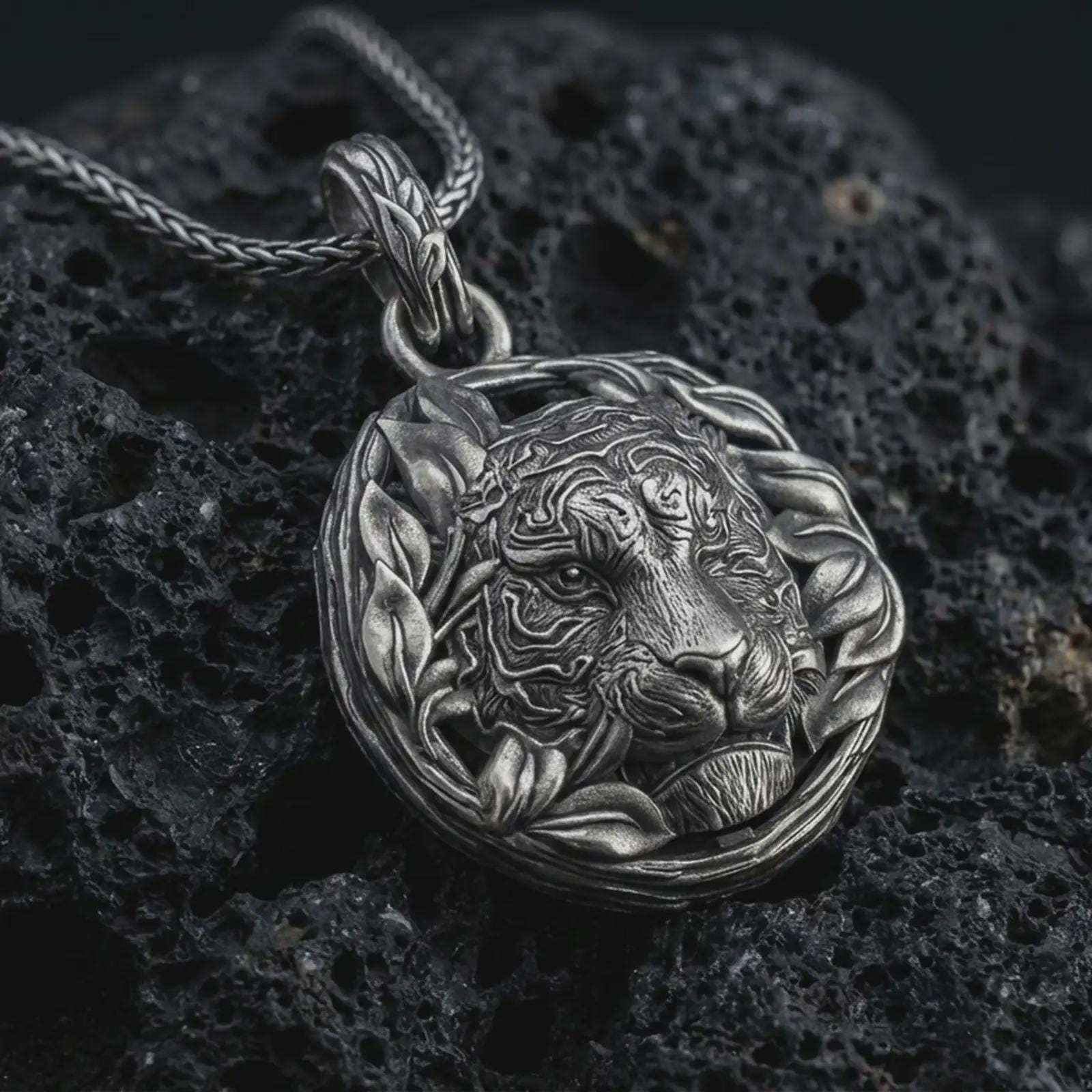 A tiger pendant on black volcanic stone with oxidized contrast highlighting the leaf wreath frame and engraved stripes.