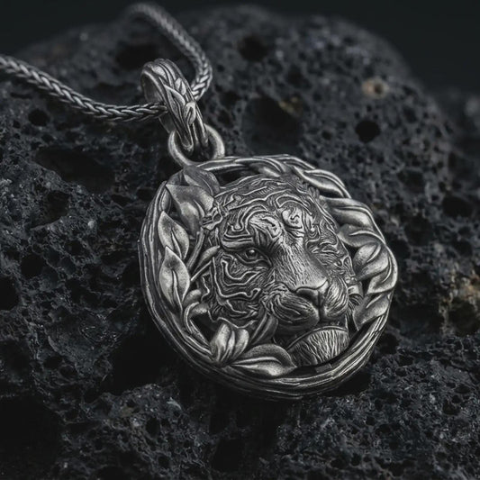 A tiger pendant on black volcanic stone with oxidized contrast highlighting the leaf wreath frame and engraved stripes.