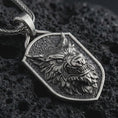 Load image into Gallery viewer, Sterling silver ferocious wolf shield pendant necklace with an oxidized finish resting on textured volcanic rock, captured in a close-up premium studio composition.
