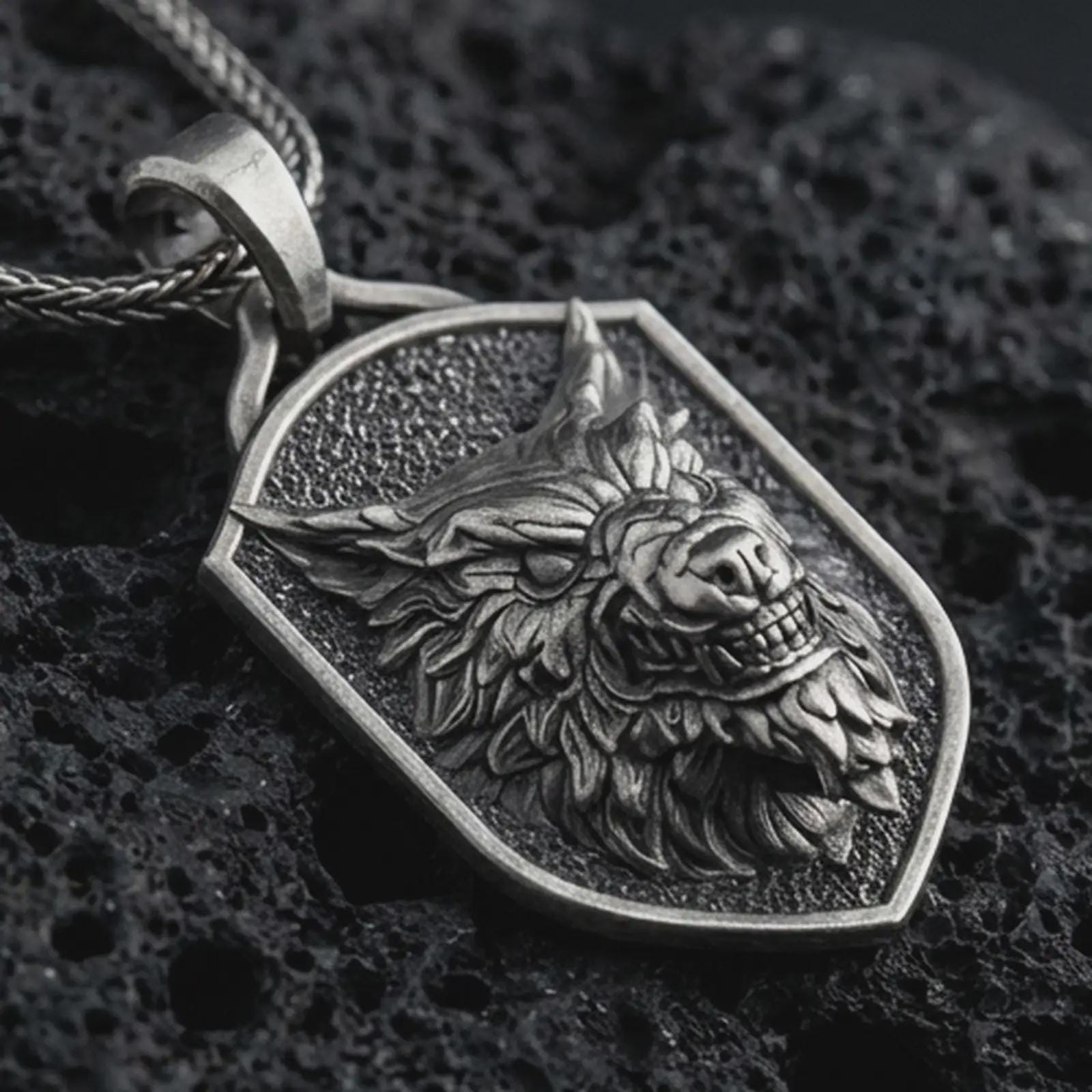 Sterling silver ferocious wolf shield pendant necklace with an oxidized finish resting on textured volcanic rock, captured in a close-up premium studio composition.