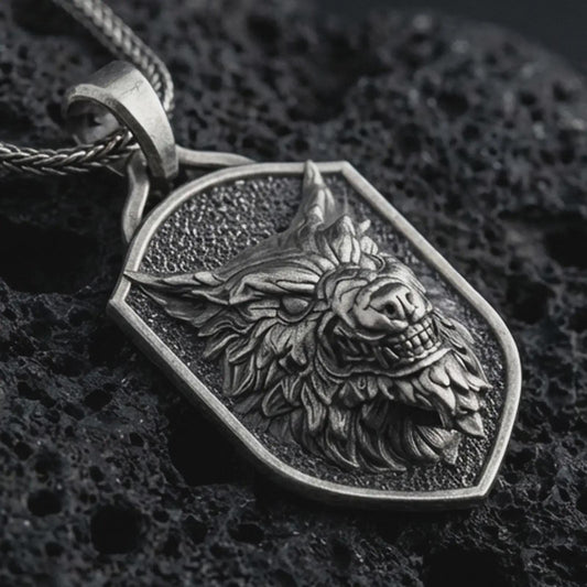 Sterling silver ferocious wolf shield pendant necklace with an oxidized finish resting on textured volcanic rock, captured in a close-up premium studio composition.
