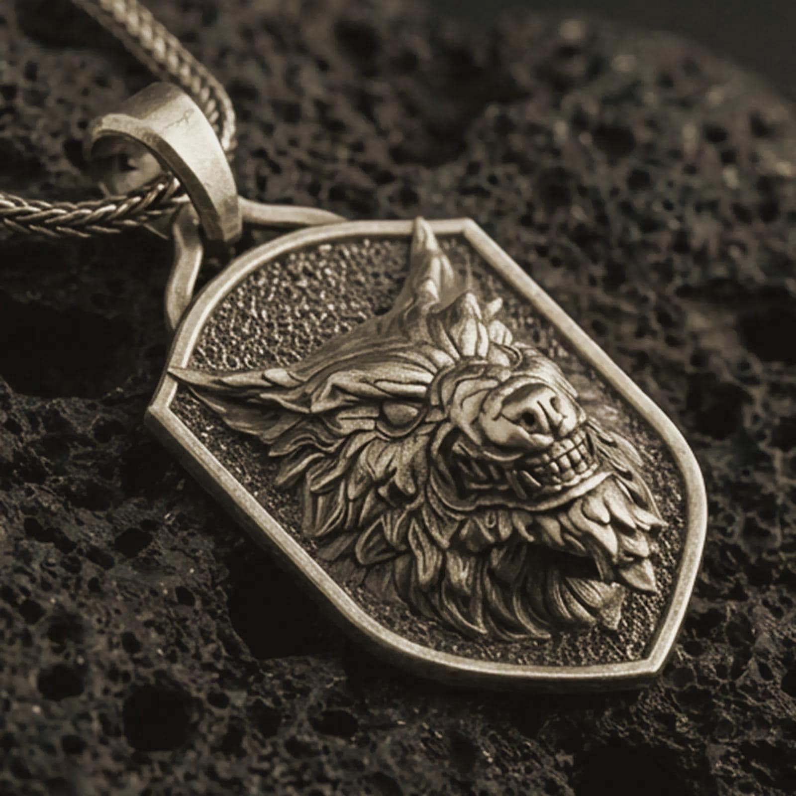 Bronze ferocious wolf shield pendant necklace with an oxidized finish resting on textured volcanic rock, captured in a close-up premium studio composition.