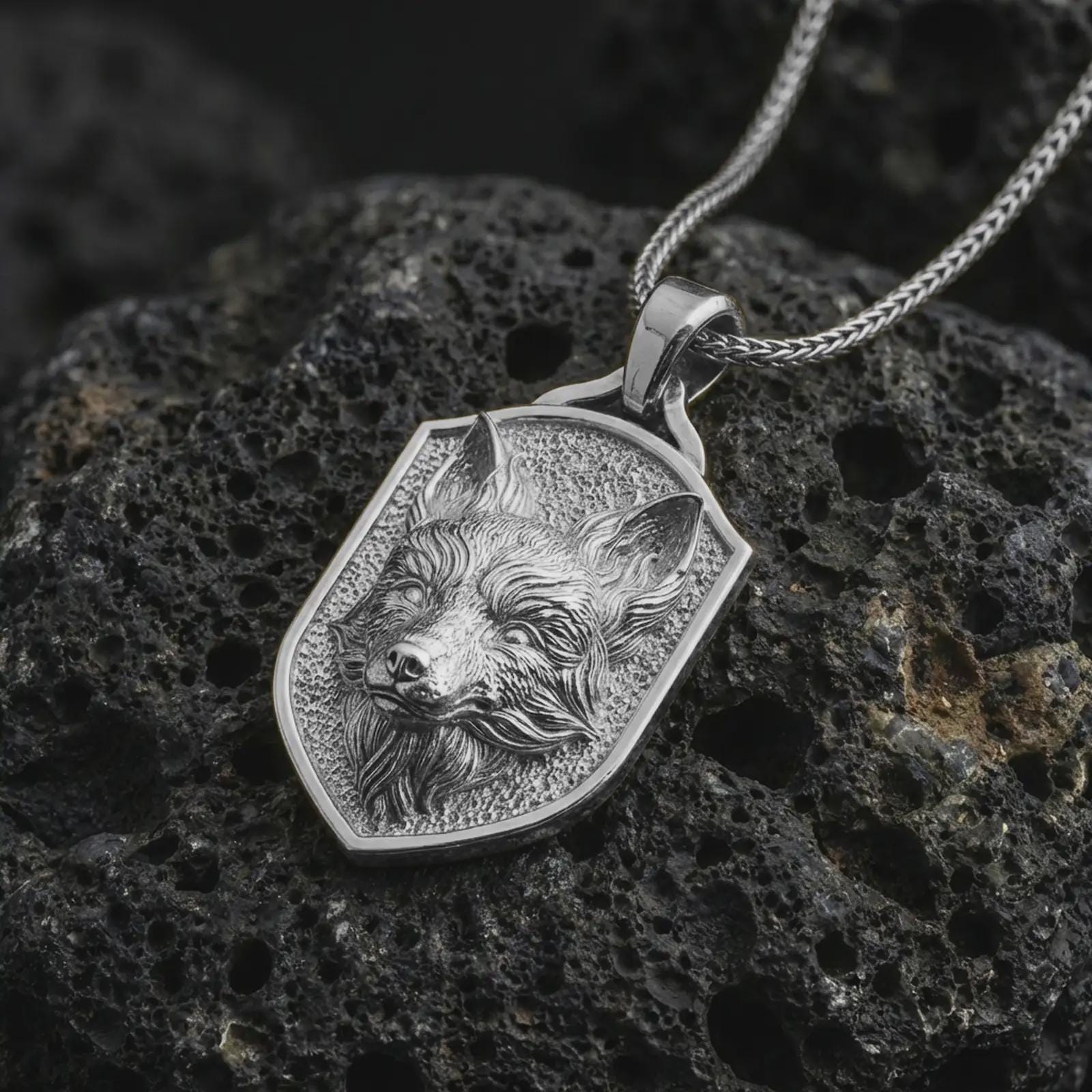 Polished silver fox shield pendant necklace displayed on black volcanic rock, shown in a refined macro product shot with alert fox face relief, flowing fur detail, and angular shield frame.