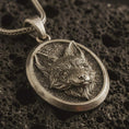 Load image into Gallery viewer, Bronze fox medallion pendant necklace with an oxidized finish resting on textured volcanic rock, captured in a close-up premium studio composition.
