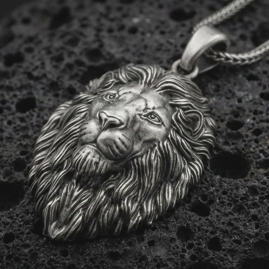 Sterling silver lion head pendant necklace with an oxidized finish resting on textured volcanic rock, captured in a close-up premium studio composition.
