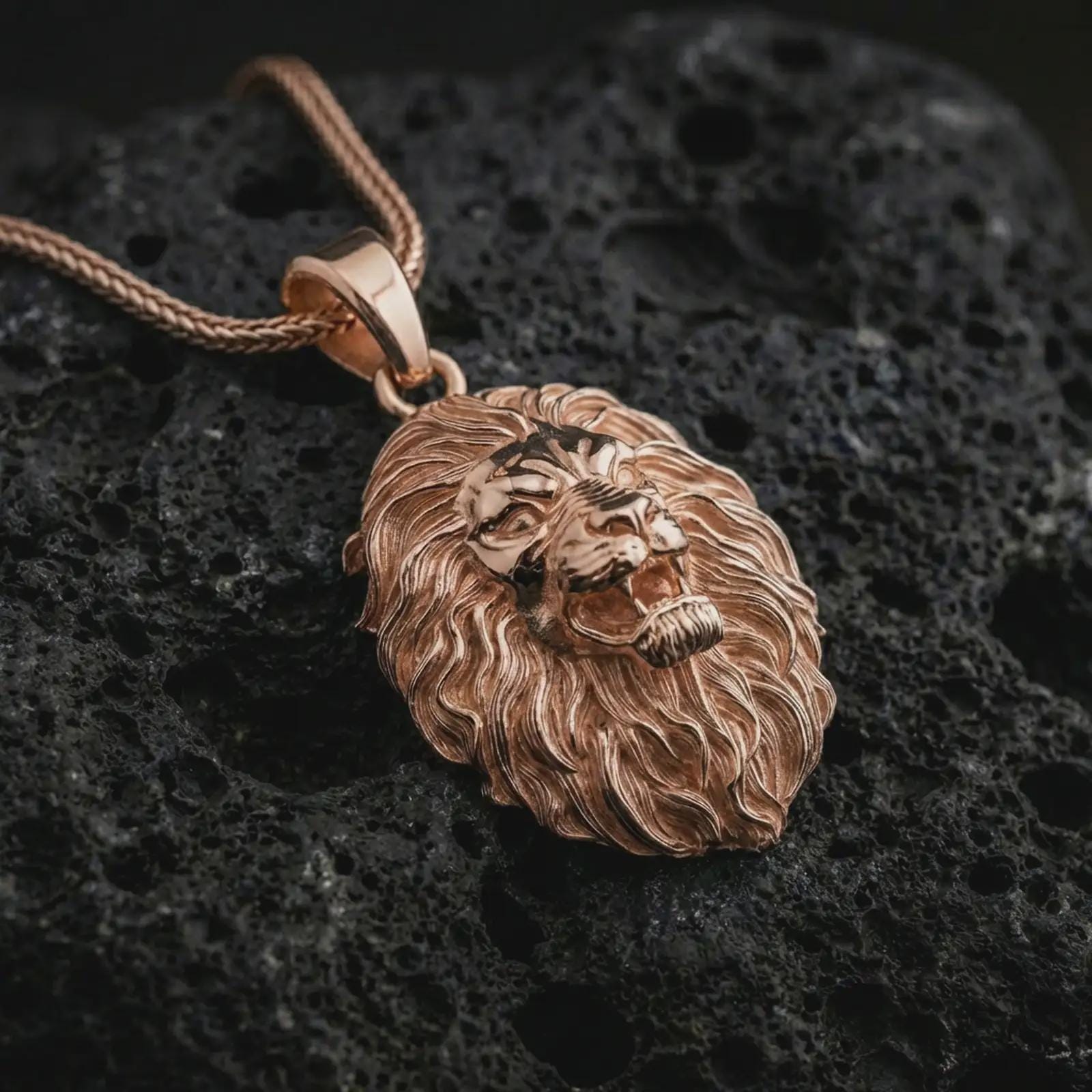Rose gold plated roaring lion head pendant necklace on dark volcanic rock, photographed in a detailed premium studio macro view.