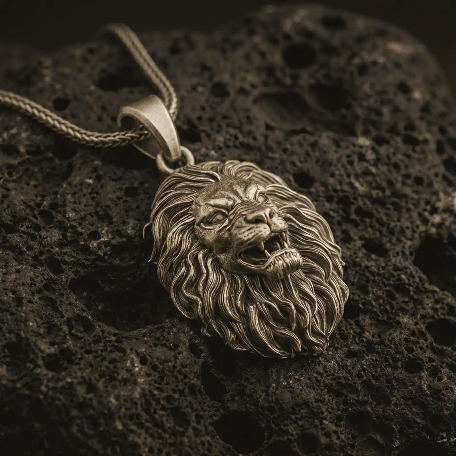 Bronze roaring lion head pendant necklace with an oxidized finish resting on textured volcanic rock, captured in a close-up premium studio composition.