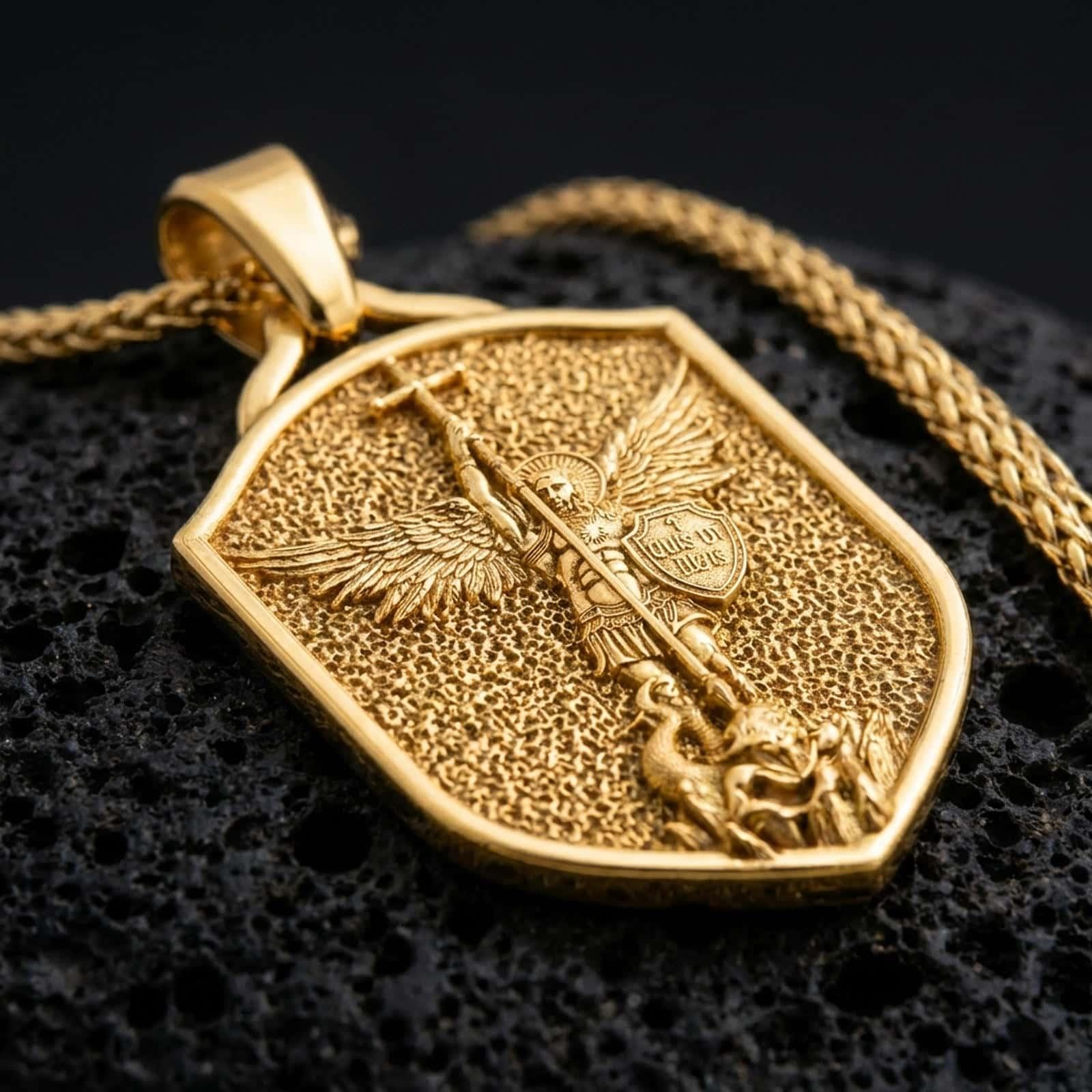 Gold plated Saint Michael shield pendant necklace presented on porous volcanic rock, highlighting the heraldic shape and sacred defender design in a luxurious close-up jewelry image.