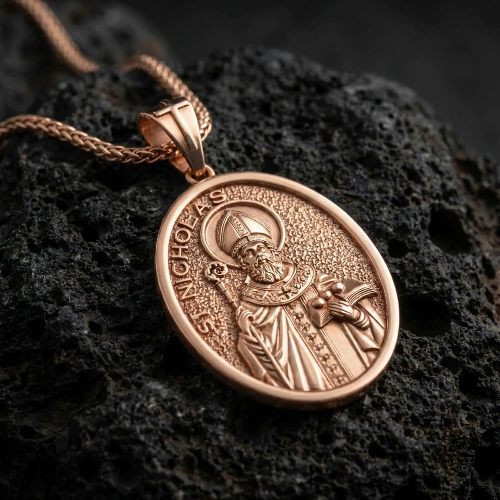 Rose gold plated Saint Nicholas pendant necklace on dark volcanic rock, photographed in a detailed premium studio macro view.