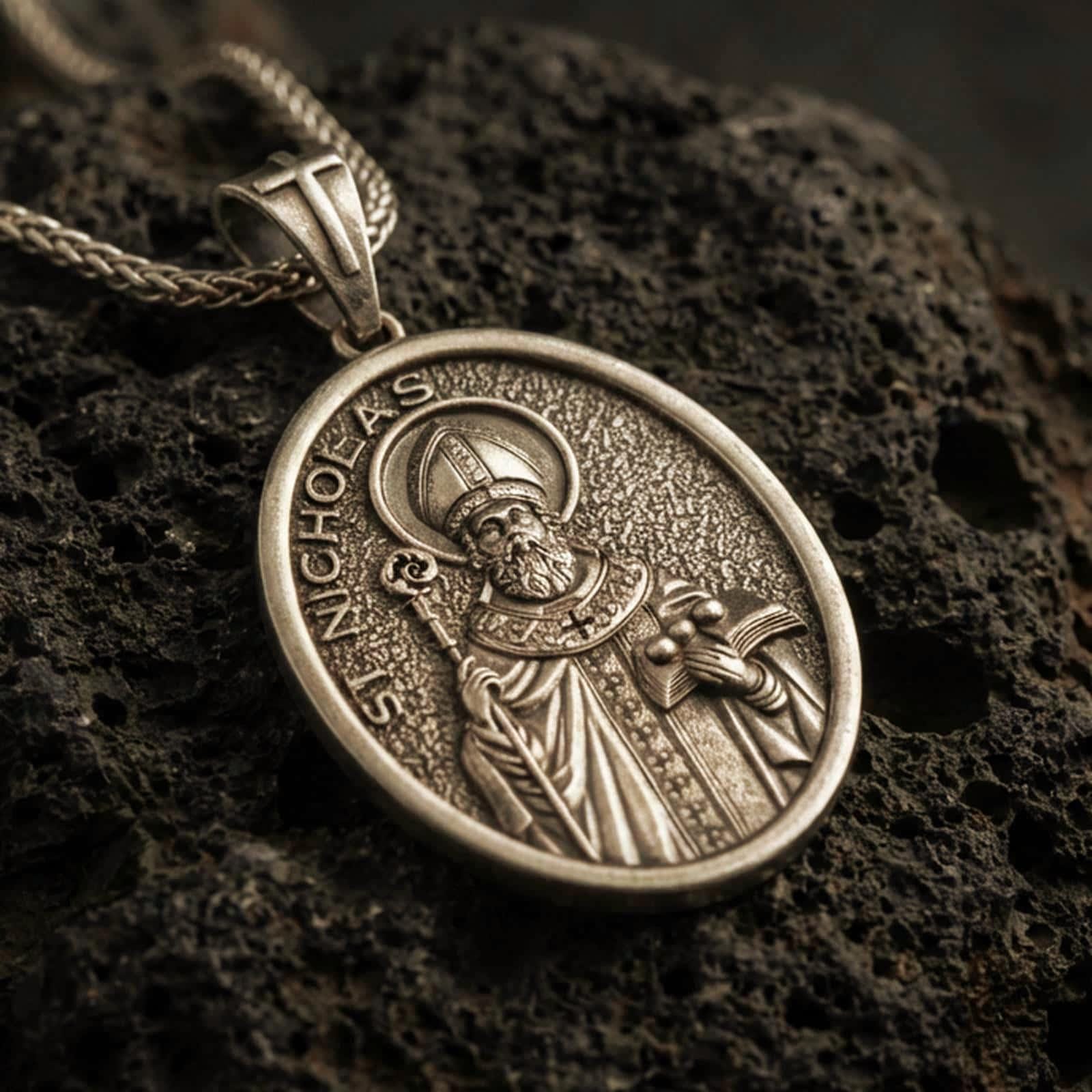 Bronze Saint Nicholas pendant necklace with an oxidized finish resting on textured volcanic rock, captured in a close-up premium studio composition.