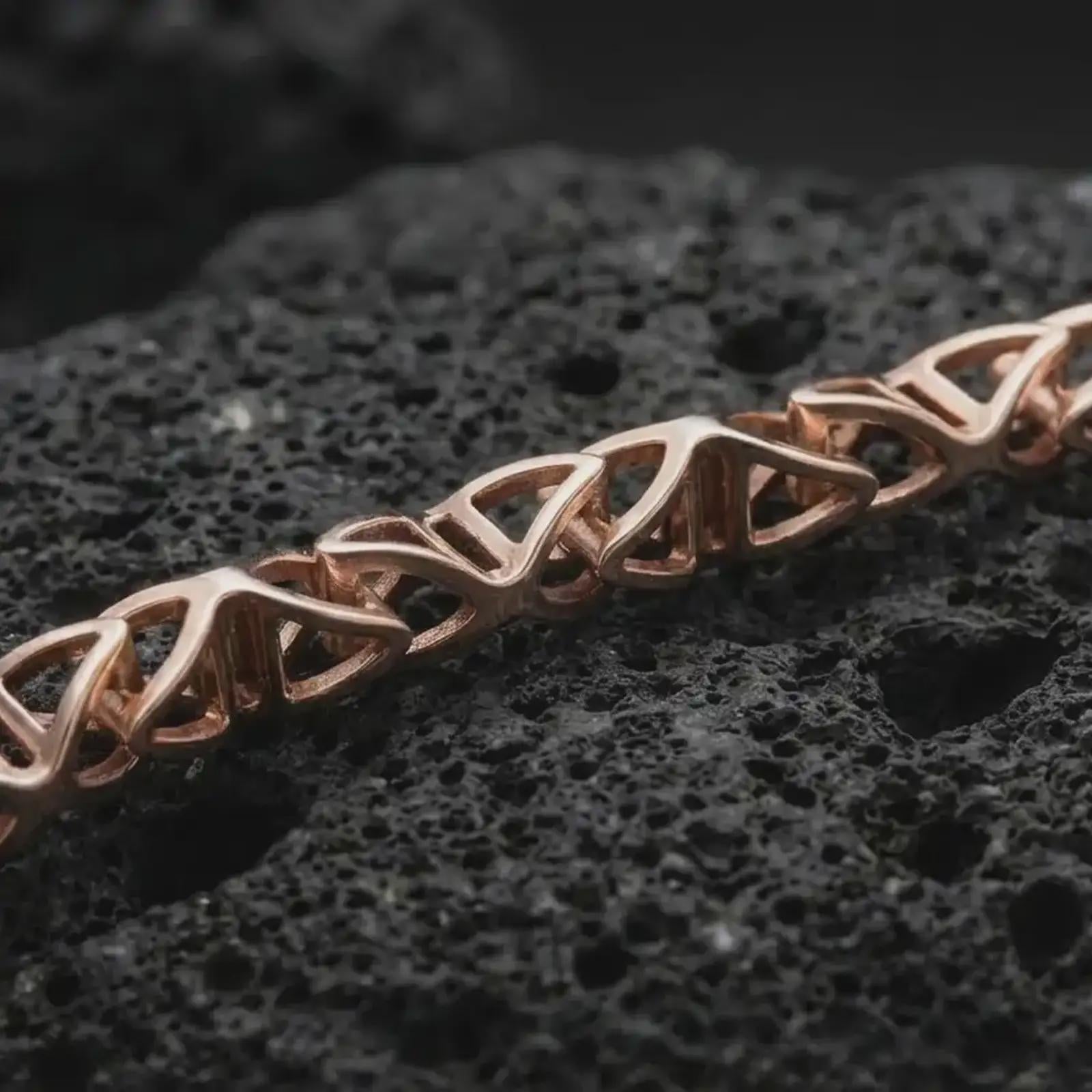 Rose gold plated DNA helix chain necklace on dark volcanic rock, photographed in a detailed premium studio macro view.