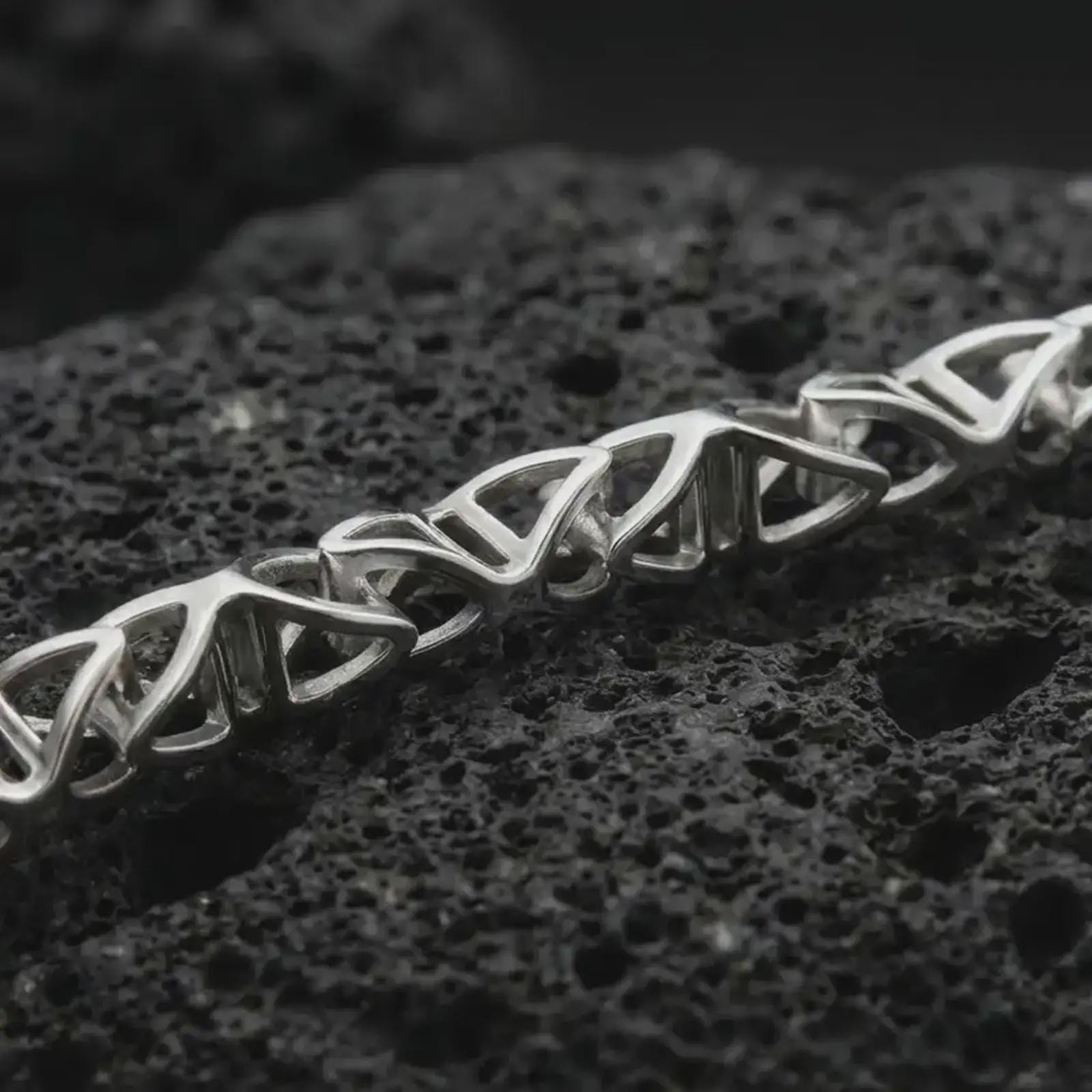 Polished silver DNA helix chain necklace displayed on black volcanic rock, shown in a refined macro product shot with interlocking molecular links and clean scientific design.