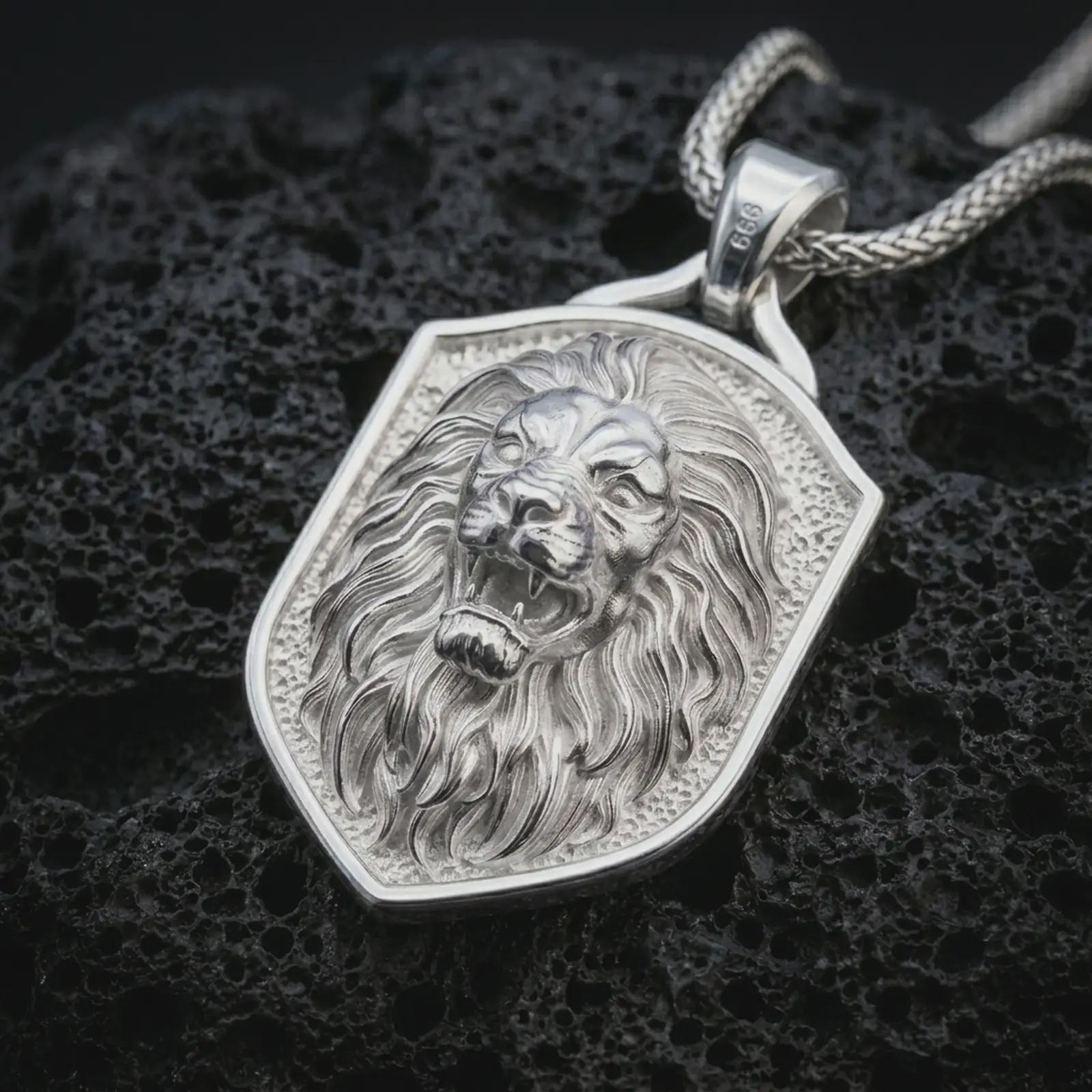 Polished silver roaring lion shield pendant necklace displayed on black volcanic rock, shown in a refined macro product shot with open mouth, fang detail, flowing mane, and angular shield frame.