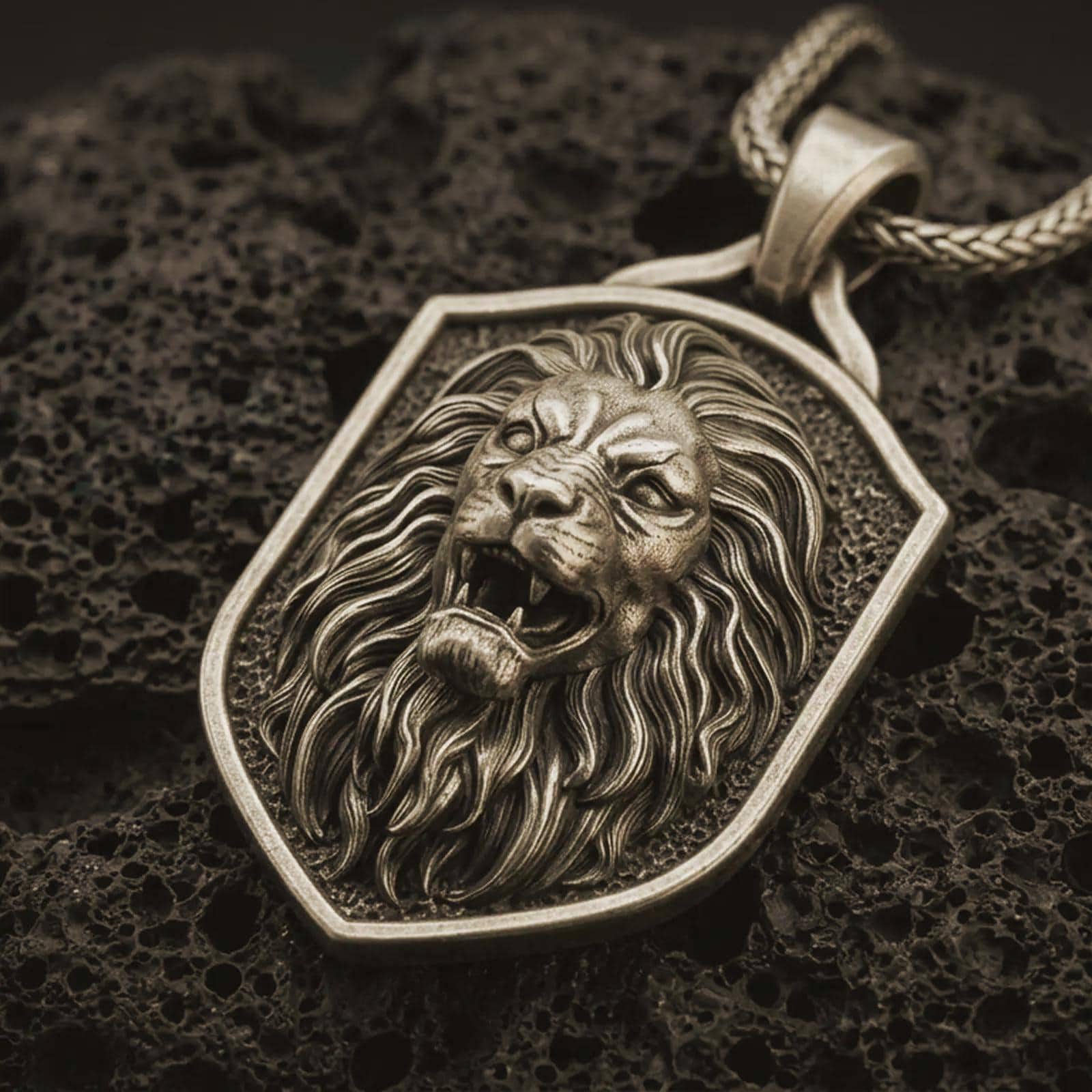 Bronze roaring lion shield pendant necklace with an oxidized finish resting on textured volcanic rock, captured in a close-up premium studio composition.