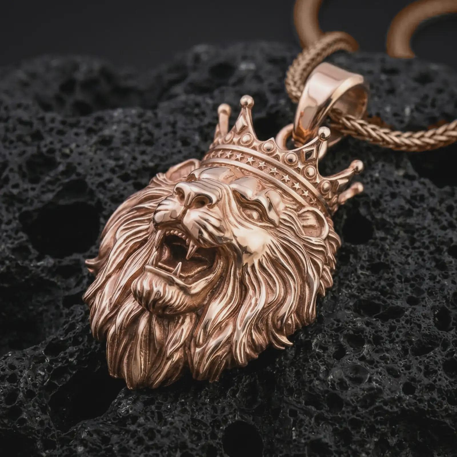 Rose gold plated crowned lion head pendant necklace on dark volcanic rock, photographed in a detailed premium studio macro view.