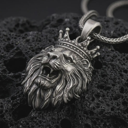Sterling silver crowned lion head pendant necklace with an oxidized finish resting on textured volcanic rock, captured in a close-up premium studio composition.