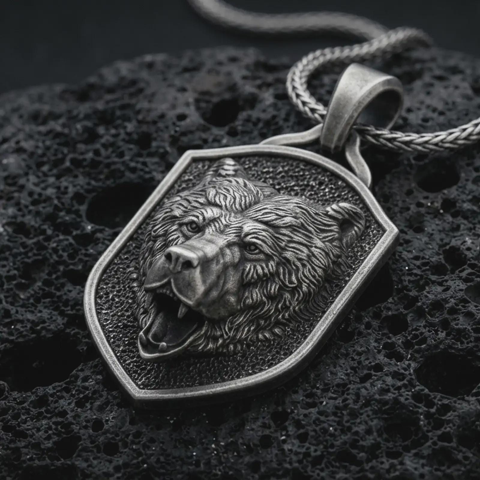 Sterling silver roaring bear shield pendant necklace with an oxidized finish resting on textured volcanic rock, captured in a close-up premium studio composition.