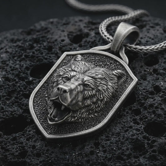 Sterling silver roaring bear shield pendant necklace with an oxidized finish resting on textured volcanic rock, captured in a close-up premium studio composition.