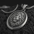 Load image into Gallery viewer, Sterling silver lion medallion pendant necklace with an oxidized finish resting on textured volcanic rock, captured in a close-up premium studio composition.
