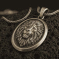 Load image into Gallery viewer, Bronze lion medallion pendant necklace with an oxidized finish resting on textured volcanic rock, captured in a close-up premium studio composition.
