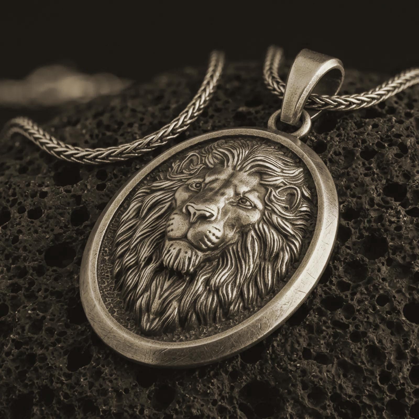 Bronze lion medallion pendant necklace with an oxidized finish resting on textured volcanic rock, captured in a close-up premium studio composition.