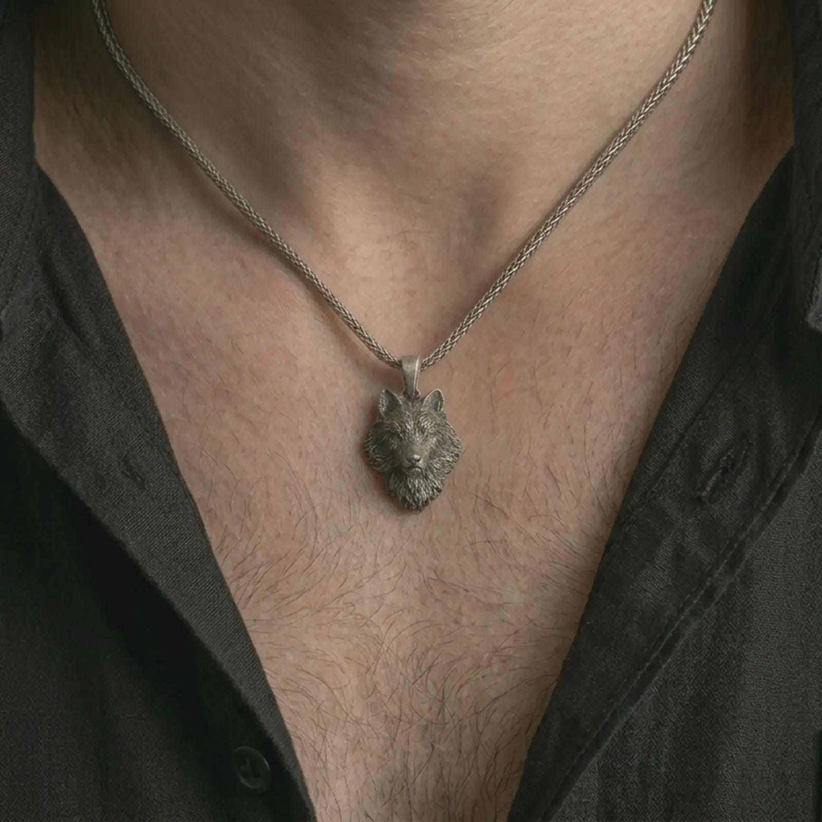 Oxidized wolf head pendant necklace worn on the neck, styled in a dark lifestyle portrait with an open shirt and bold nature-inspired presentation.