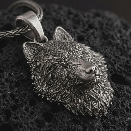 Sterling silver wolf head pendant necklace with an oxidized finish resting on textured volcanic rock, captured in a close-up premium studio composition.