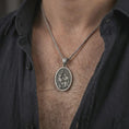 Load image into Gallery viewer, Oxidized Saint Hubert pendant necklace worn on the neck, styled in a dark lifestyle portrait with an open shirt and masculine presentation.
