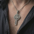 Load image into Gallery viewer, Oxidized Celtic cross pendant necklace worn on the neck, styled in a dark lifestyle portrait with an open shirt and masculine presentation.
