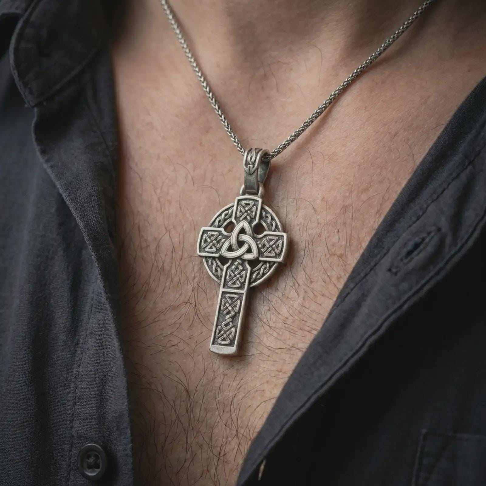 Oxidized Celtic cross pendant necklace worn on the neck, styled in a dark lifestyle portrait with an open shirt and masculine presentation.