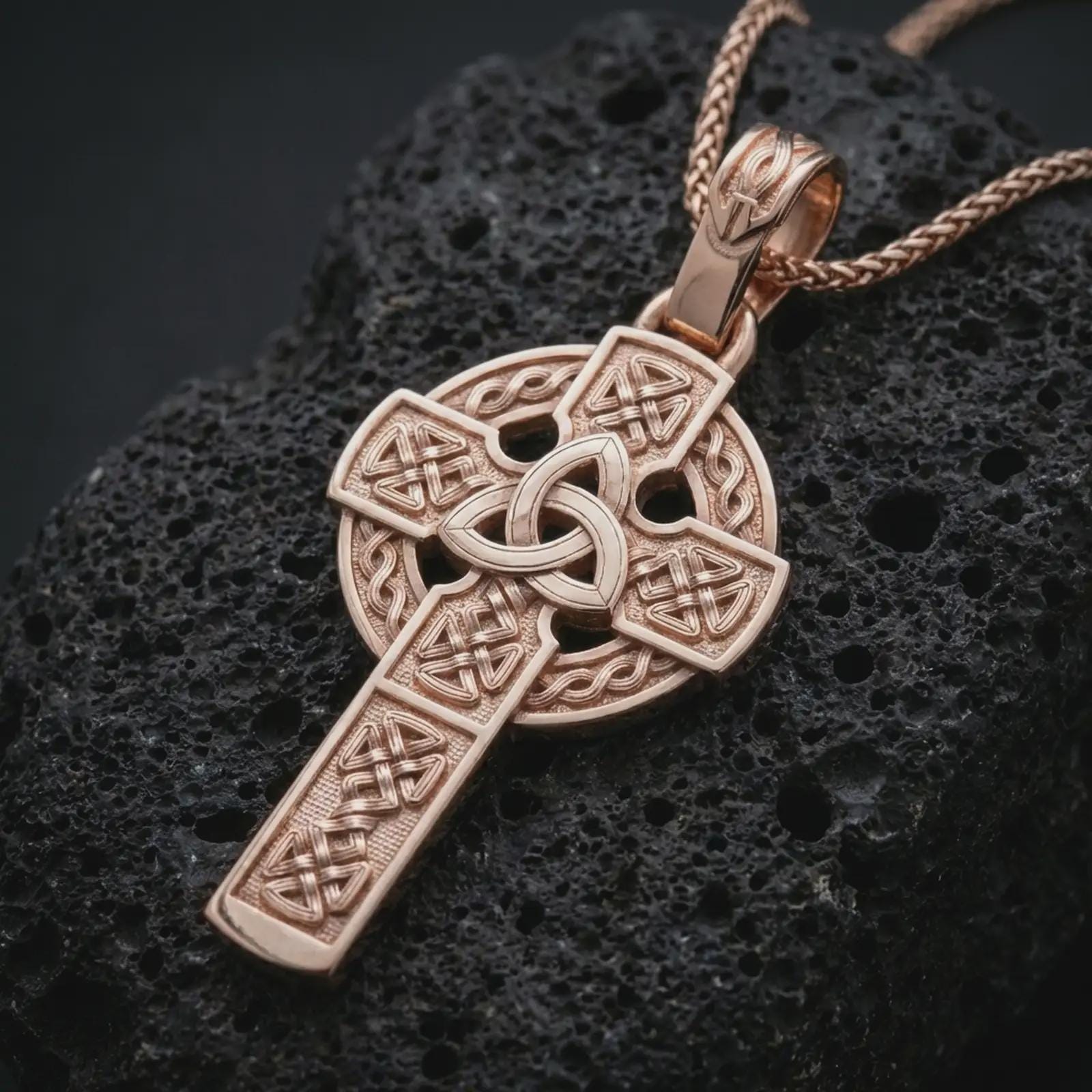 Rose gold plated Celtic cross pendant necklace on dark volcanic rock, photographed in a detailed premium studio macro view.