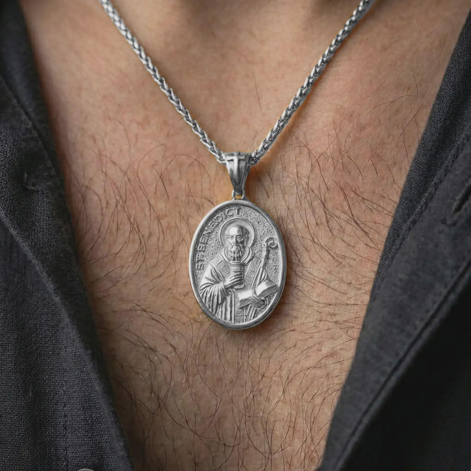 Polished silver Saint Benedict pendant necklace worn on the neck, shown against the chest in a clean and elegant everyday wear composition.