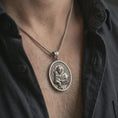 Load image into Gallery viewer, Oxidized Saint Anthony pendant necklace worn on the neck, styled in a dark lifestyle portrait with an open shirt and masculine presentation.
