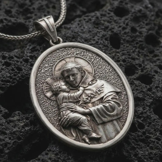 Sterling silver Saint Anthony pendant necklace with an oxidized finish resting on textured volcanic rock, captured in a close-up premium studio composition.