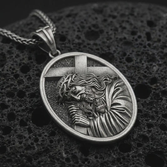 Sterling silver Jesus carrying cross pendant necklace with an oxidized finish resting on textured volcanic rock, captured in a close-up premium studio composition.