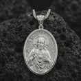 Load image into Gallery viewer, Polished silver Jesus Christ pendant necklace displayed on black volcanic rock, shown in a refined macro product shot with detailed sacred figure and engraved lettering.
