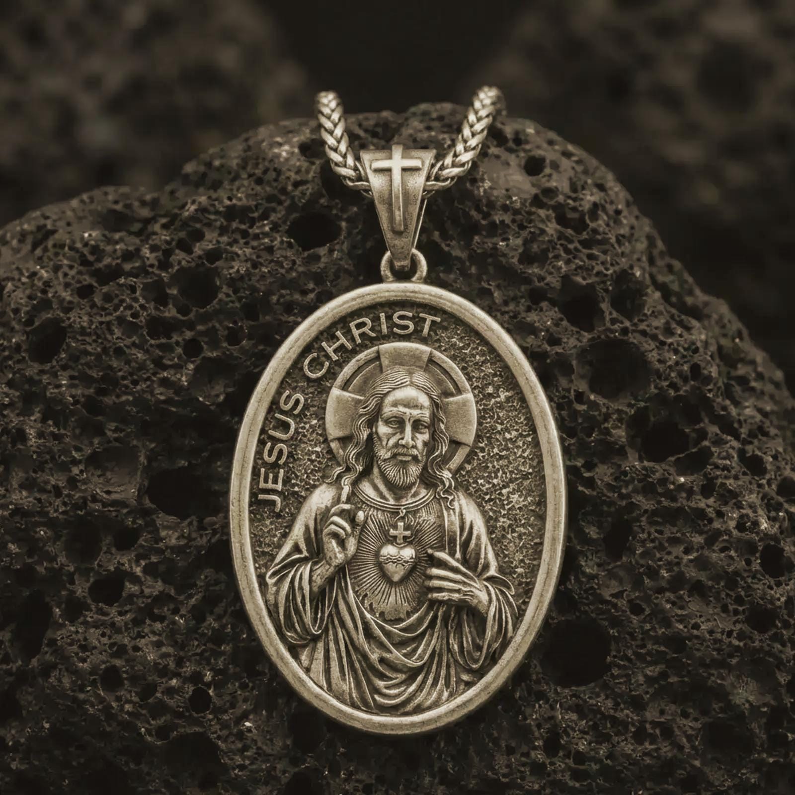 Bronze Jesus Christ pendant necklace with an oxidized finish resting on textured volcanic rock, captured in a close-up premium studio composition.