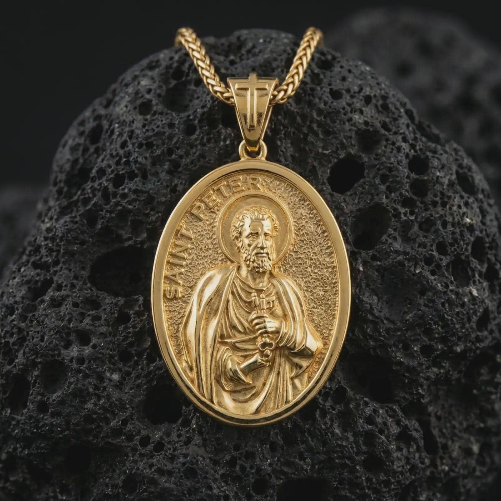 Gold plated Saint Peter pendant necklace presented on porous volcanic rock, highlighting the oval medallion form and sacred devotional design in a luxurious close-up jewelry image.