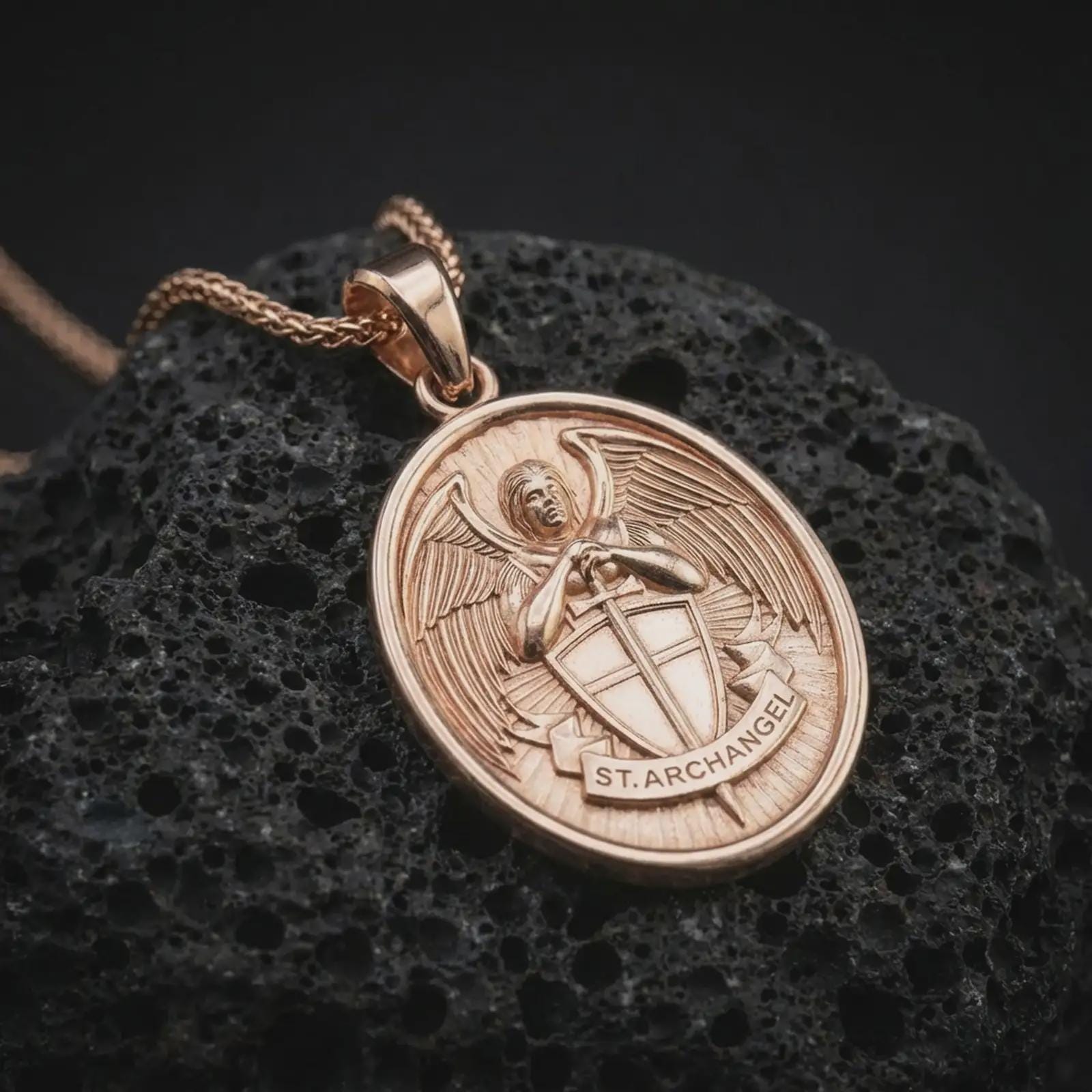 Rose gold plated Saint Michael Archangel pendant necklace on dark volcanic rock, photographed in a detailed premium studio macro view.