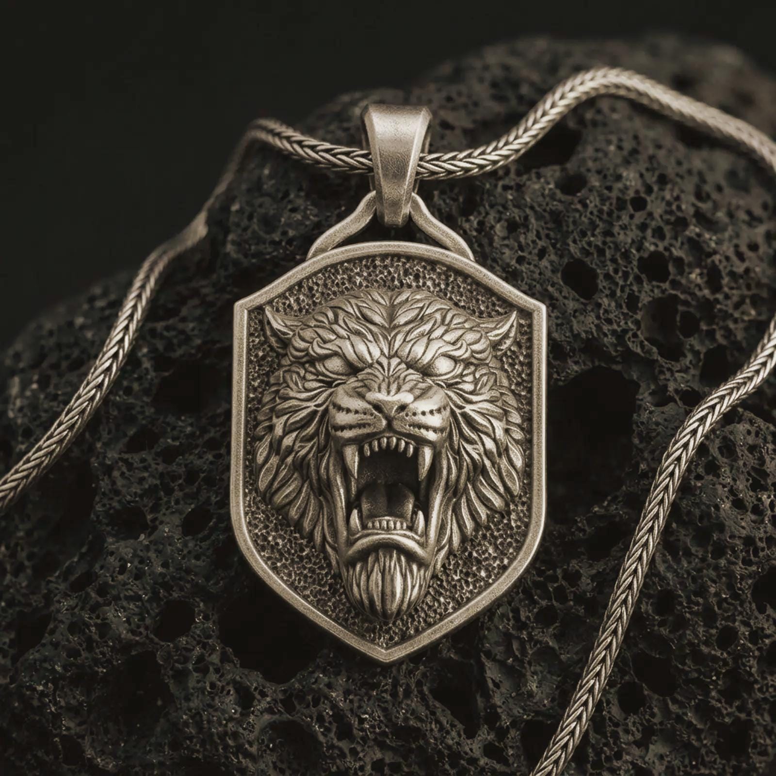 Bronze roaring lion shield pendant necklace with an oxidized finish resting on textured volcanic rock, captured in a close-up premium studio composition.