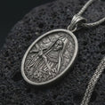 Load image into Gallery viewer, Sterling silver Saint Rita pendant necklace with an oxidized finish resting on textured volcanic rock, captured in a close-up premium studio composition.
