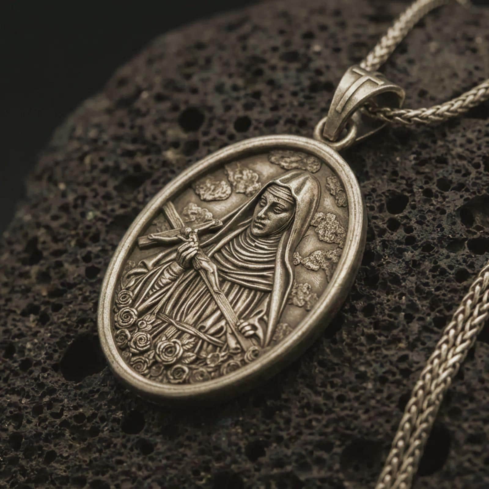 Bronze Saint Rita pendant necklace with an oxidized finish resting on textured volcanic rock, captured in a close-up premium studio composition.