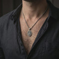 Load image into Gallery viewer, Oxidized Saint Martin of Tours pendant necklace worn on the neck, styled in a dark lifestyle portrait with an open shirt and masculine presentation.
