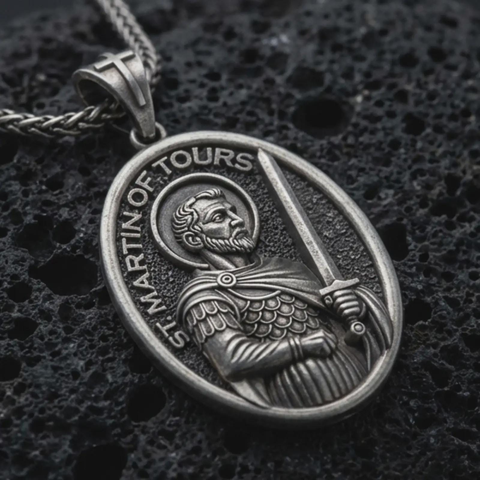 Sterling silver Saint Martin of Tours pendant necklace with an oxidized finish resting on textured volcanic rock, captured in a close-up premium studio composition.