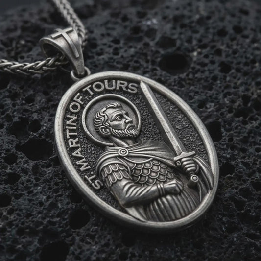Sterling silver Saint Martin of Tours pendant necklace with an oxidized finish resting on textured volcanic rock, captured in a close-up premium studio composition.