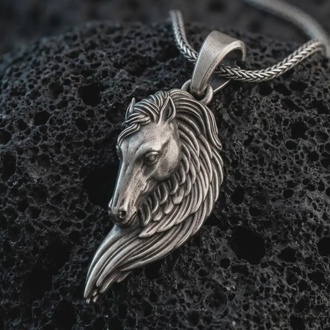 Sterling silver Pegasus wing horse pendant necklace with an oxidized finish resting on textured volcanic rock, captured in a close-up premium studio composition.