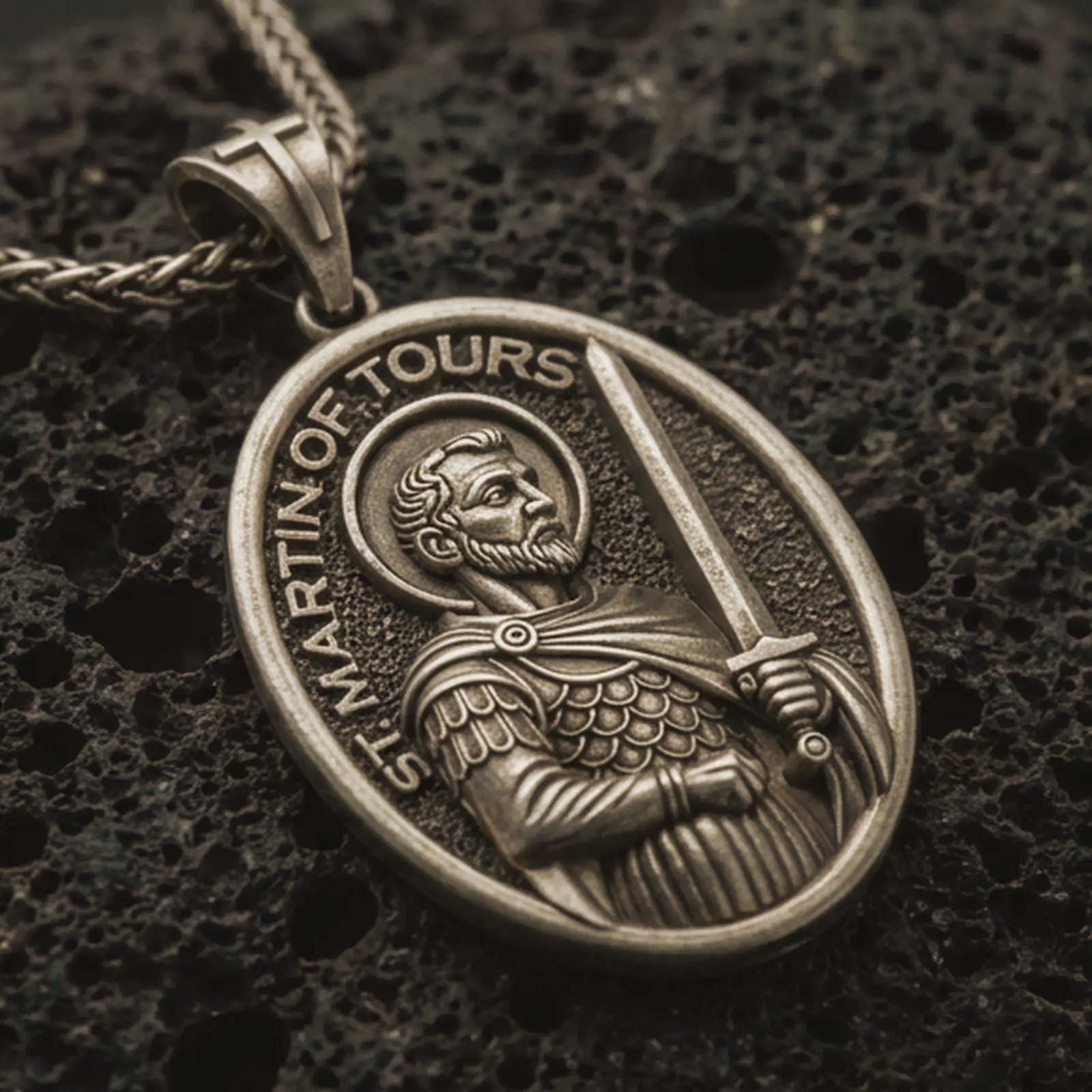 Bronze Saint Martin of Tours pendant necklace with an oxidized finish resting on textured volcanic rock, captured in a close-up premium studio composition.