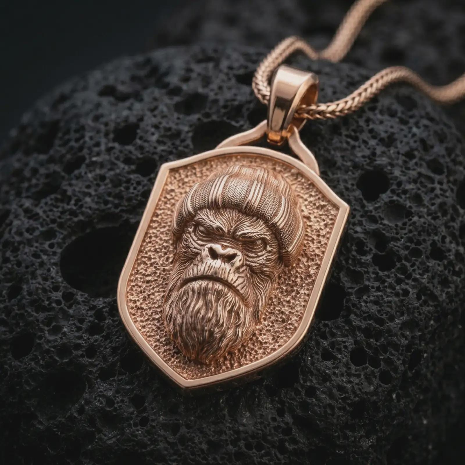 Rose gold plated gorilla shield pendant necklace on dark volcanic rock, photographed in a detailed premium studio macro view.