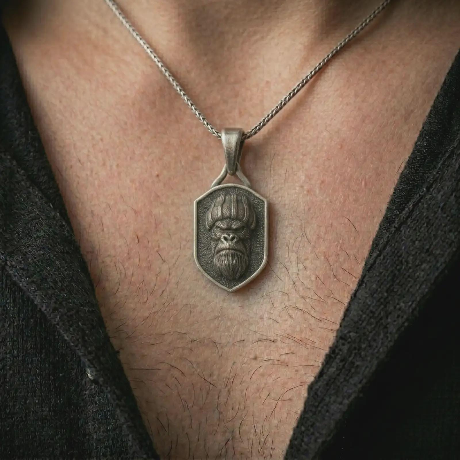 Oxidized gorilla shield pendant necklace worn on the neck, styled in a dark lifestyle portrait with an open shirt and bold street-inspired presentation.