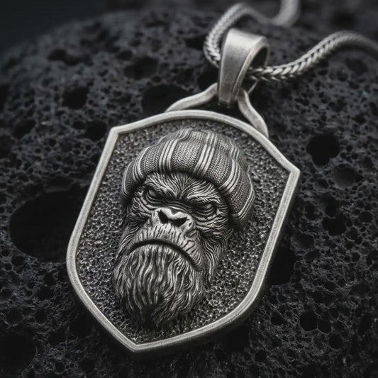 Sterling silver gorilla shield pendant necklace with an oxidized finish resting on textured volcanic rock, captured in a close-up premium studio composition.
